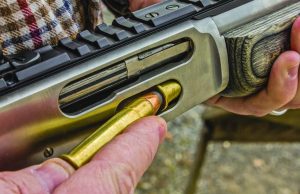 A lever action rifle with an open loading gate, demonstrating how rounds are inserted into the tubular magazine.